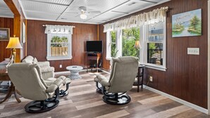A room with two reclining chairs, a TV, a ceiling fan, and a painting on the wall. - Safe Haven Cottage- Beach, Shopping, Fun! (Surf City)