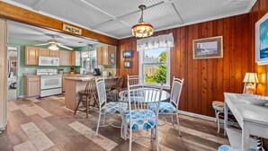 A kitchen with wooden cabinets, a microwave, and a dining area with a round table and chairs. - Safe Haven Cottage- Beach, Shopping, Fun! (Surf City)