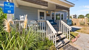 A beachfront property with a porch, outdoor seating, and a sign for Paragon Vacation Rentals. - Safe Haven Cottage- Beach, Shopping, Fun! (Surf City)