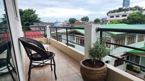 A balcony with a chair and a potted plant, overlooking a residential area with various buildings.