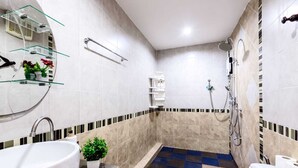 A modern bathroom with a bathtub, shower, and a small sink. There are glass shelves with toiletries and a potted plant.