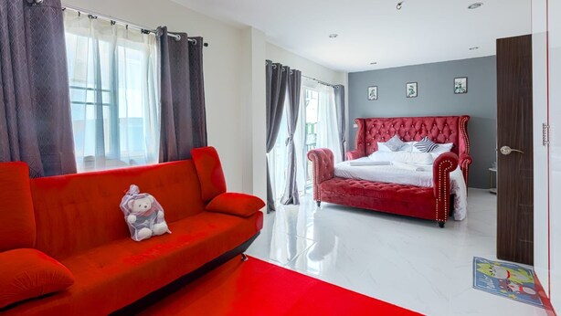 A modern bedroom with a red sofa, a red upholstered bed, and a large window with curtains.