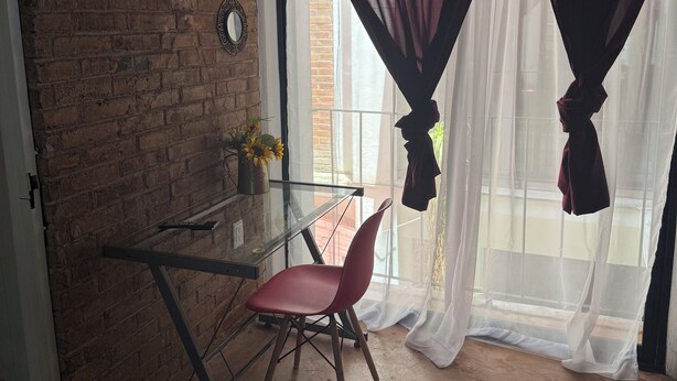 A room with a brick wall, a glass table, a red chair, and a window with sheer curtains. - Beatiful aparment in the magical town of Orizaba 2 (Orizaba)