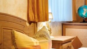 Ein Schlafzimmer mit hölzernem Kopfteil, einer Nachttischlampe, einem Globus und einem Fenster mit Vorhängen.