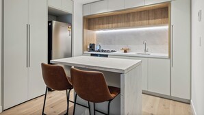 A modern kitchen with a central island, two bar stools, a built-in oven, and a wooden backsplash. - Spacious City Retreat with Study (Victoria)