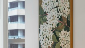 A modern interior with a large painting of white flowers on the wall, a round table, and a brown chair. - Spacious City Retreat with Study (Victoria)