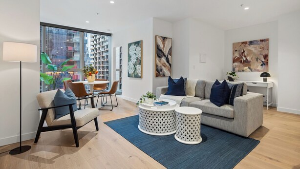 A modern living room with a sofa, armchair, coffee table, and side tables. There is a large window with a view of a cityscape. - Spacious City Retreat with Study (Victoria)
