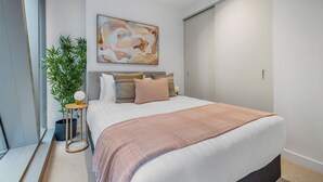 A modern bedroom with a large bed, a wall-mounted abstract painting, a potted plant, and a bedside table with a lamp. - Spacious City Retreat with Study (Victoria)