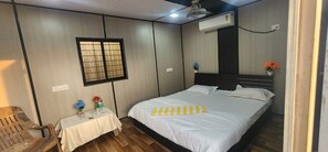 A hotel room with a bed, a small table with flowers, a chair, and an air conditioning unit. - Aviator Resort (Arambol)