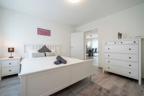 Un dormitorio con cama, mesitas de noche, cómoda y puerta que da a otra habitación.
