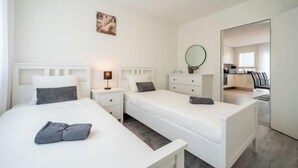 Habitación de hotel con dos camas individuales, una mesita de noche con lámpara, un aparador y un espejo.