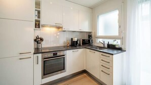Una cocina moderna con armarios blancos, horno empotrado, microondas y cafetera.