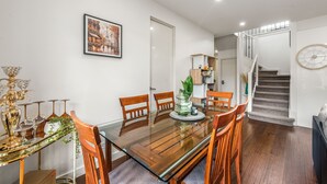 A dining area with a glass-top table, wooden chairs, a vase with a plant, and a framed picture on the wall. - Stylish Modern 3BR Townhouse in Camberwell near Train,Tram& Shops (Camberwell)