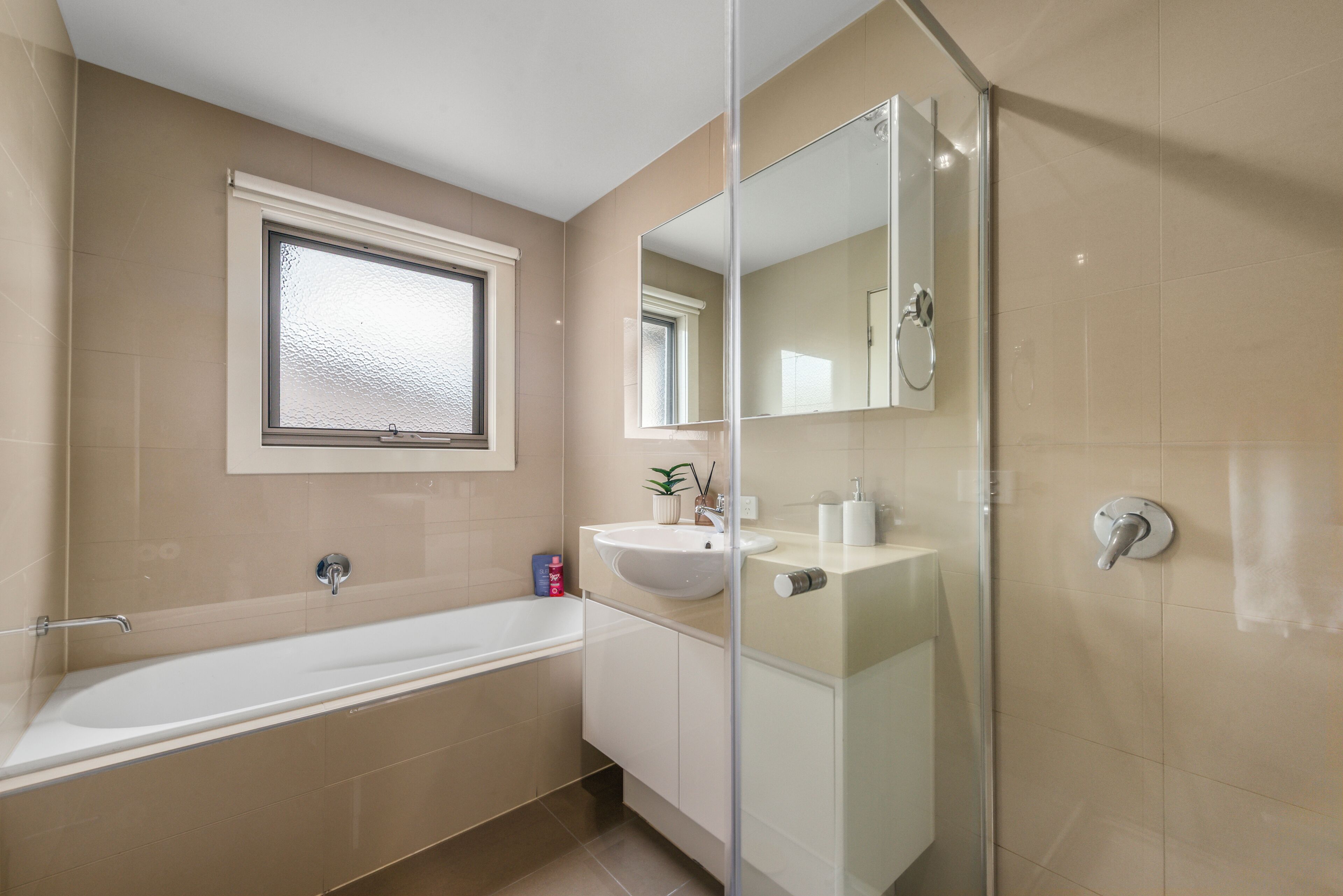 A modern bathroom with a bathtub, a sink, a mirror, and a window.