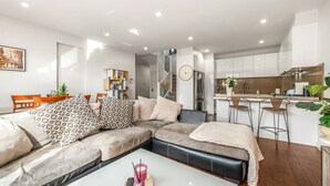 A modern living room with a sectional sofa, a coffee table, and a kitchen area with bar stools. - Stylish Modern 3BR Townhouse in Camberwell near Train,Tram& Shops (Camberwell)