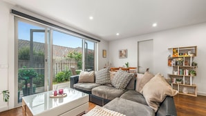 A modern living room with a sectional sofa, a glass coffee table, and a bookshelf. - Stylish Modern 3BR Townhouse in Camberwell near Train,Tram& Shops (Camberwell)