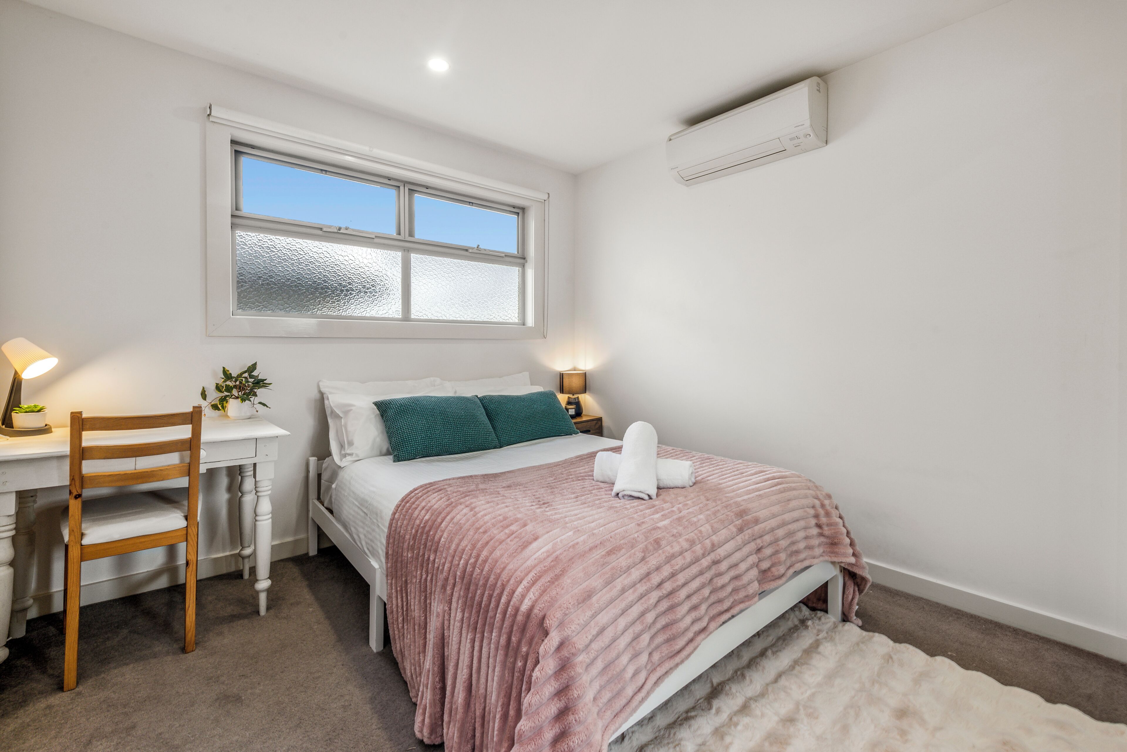Une chambre à coucher avec un lit, un bureau, une chaise, une fenêtre et un climatiseur.