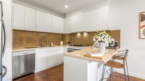 A modern kitchen with white cabinetry, a wooden countertop, a built-in dishwasher, and a small island with bar stools. - Stylish Modern 3BR Townhouse in Camberwell near Train,Tram& Shops (Camberwell)