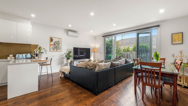 A modern living room with a sofa, dining table, and kitchen area. - Stylish Modern 3BR Townhouse in Camberwell near Train,Tram& Shops (Camberwell)
