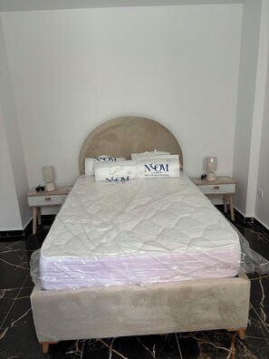 A neatly made bed with a headboard, two bedside tables with lamps, and a bedside table with a bottle and glasses.