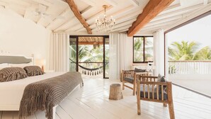 A bedroom with a large bed, a wooden chair, a hammock, and a balcony with a view of palm trees. - Villa La Semilla • 5BR Beachfront w/ Chef (Tulum)