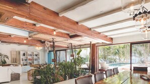 A spacious dining area with a long wooden table, surrounded by chairs, and a view of a pool and greenery outside. - Villa La Semilla • 5BR Beachfront w/ Chef (Tulum)