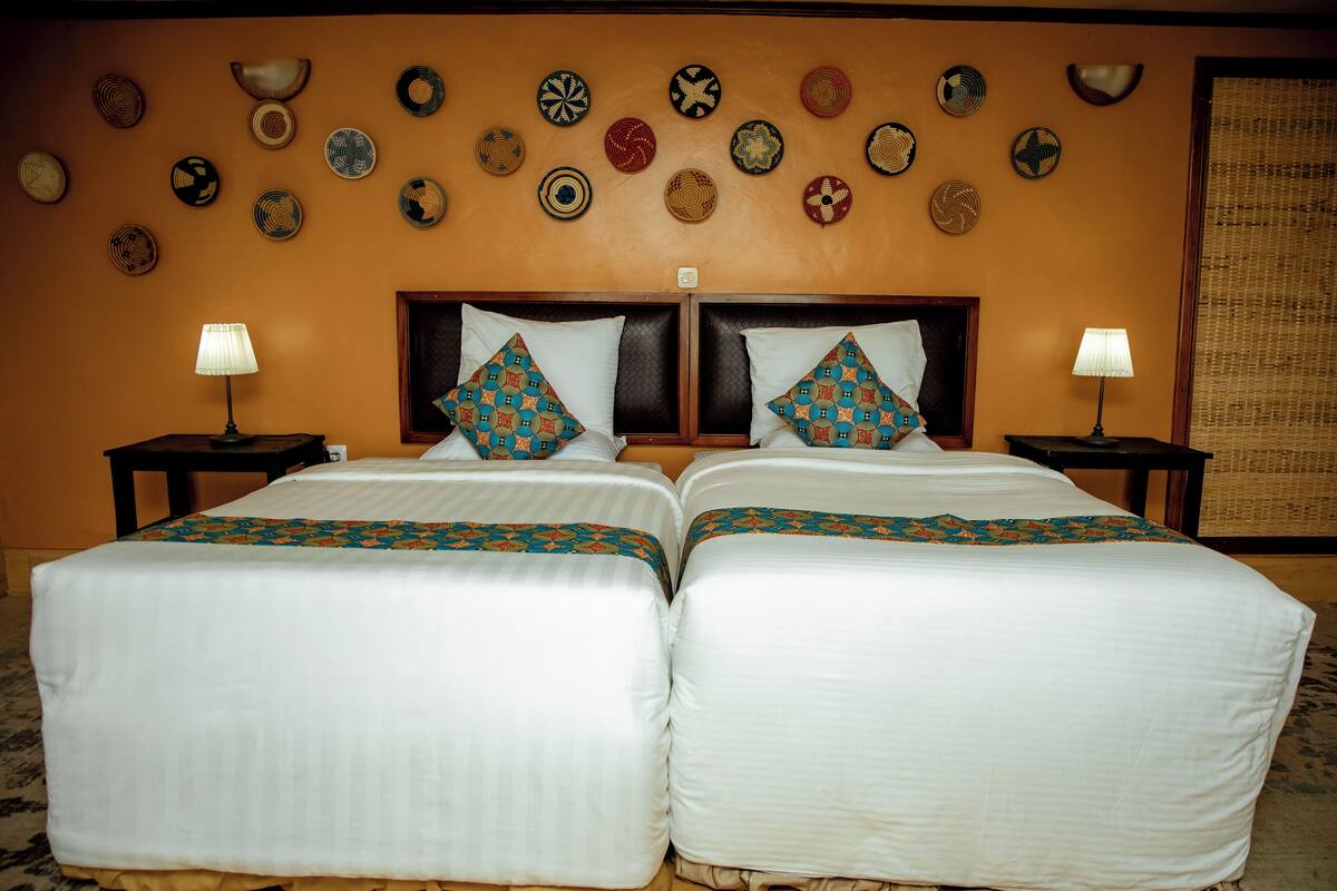 A double bed with a patterned bedspread and pillows, two bedside tables with lamps, and a wall decorated with circular woven art pieces.