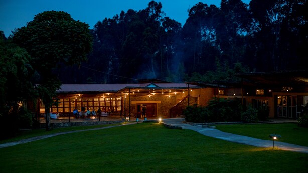 A building with a large glass facade, a covered outdoor seating area, and a well-maintained lawn. - Mountain Gorilla View Lodge (Kinigi)