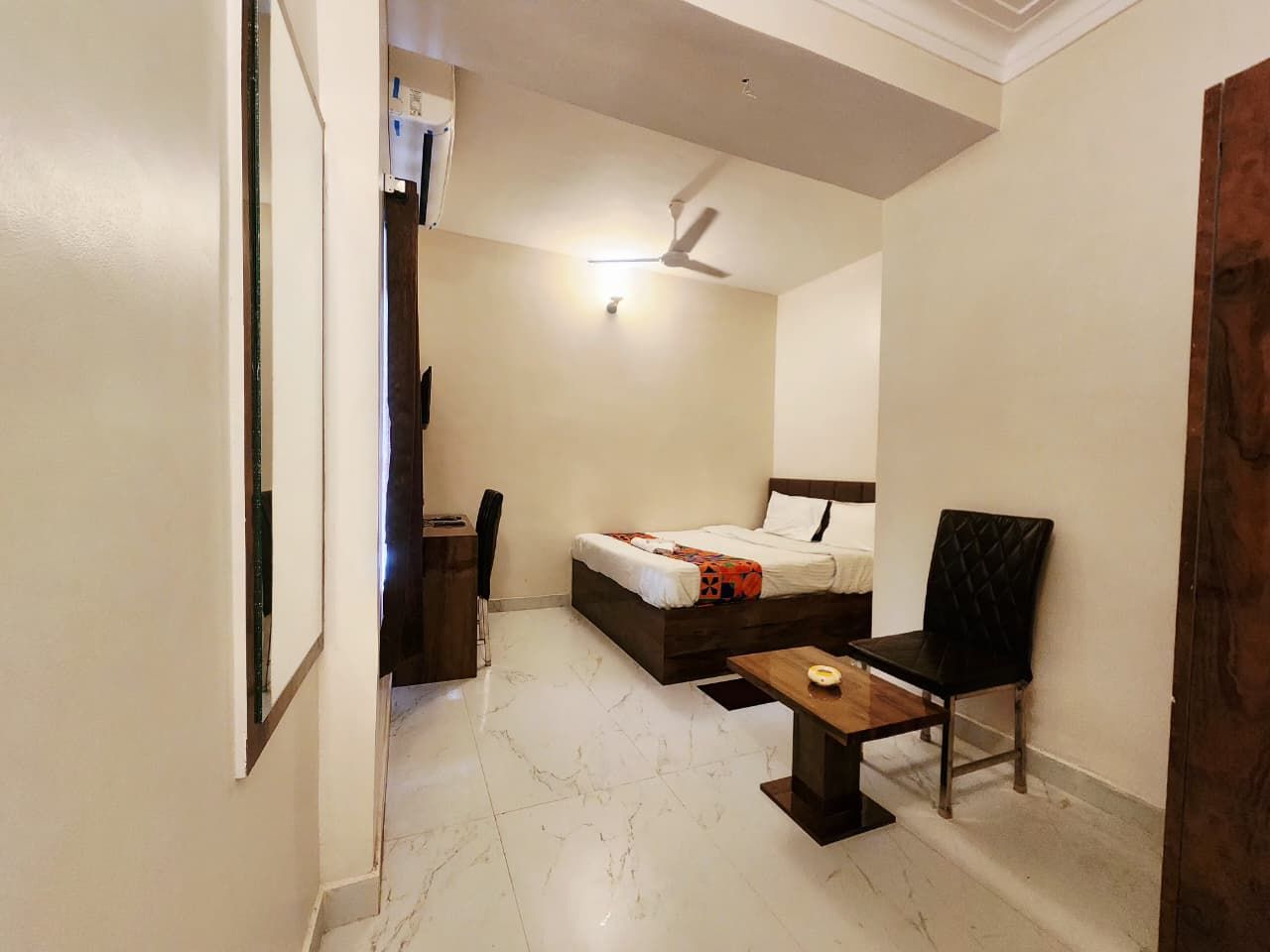 A hotel room with a bed, a desk, a chair, and a ceiling fan.