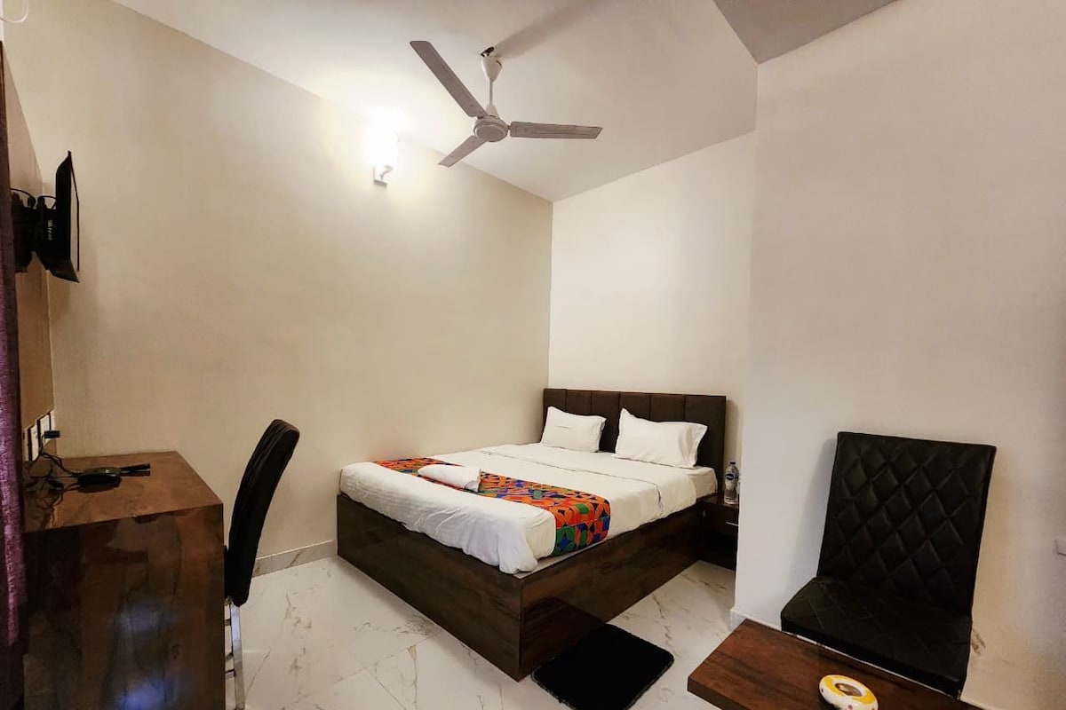 A bedroom with a bed, a desk, a chair, a ceiling fan, and a small table.
