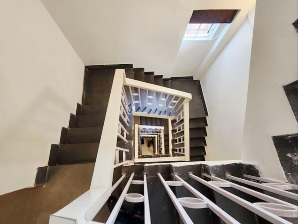 Una escalera con barandal blanco, un tragaluz en la parte superior y un piso oscuro.