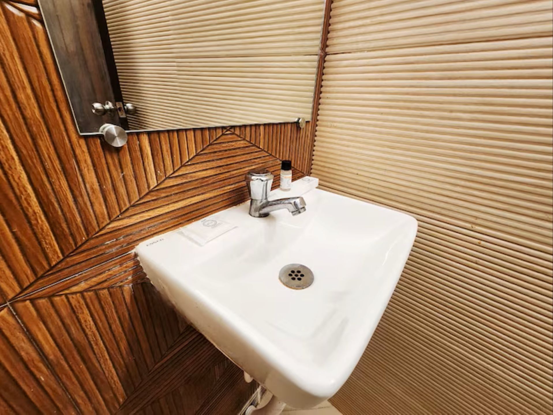 A bathroom with a wooden panel wall, a white sink, and a mirror.