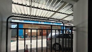 Einfahrt zu einer Parkgarage mit Metallgitter, überdachter Fläche und einem Gebäude mit blauer Tür im Hintergrund.