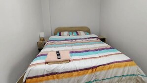 Ein Einzelbett mit gestreifter Bettdecke, ein Holz-Kopfteil, ein Nachttisch mit Lampe und ein kleiner Tisch mit Telefon und Buch.