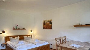 A room with a wooden bed, bedside tables, a wooden dining table with chairs, and wall-mounted shelves. - Apartment 38 sqm living/bedroom and terrace, App. 4 (Aschau im Chiemgau)