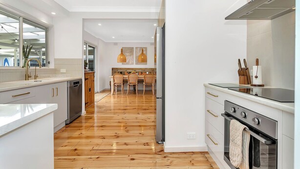 A modern kitchen with wooden flooring, white cabinetry, and stainless steel appliances. - Daisy's Beachside Cottage-Picnic Garden, Pool Table & Games in Port Noarlunga (Port Noarlunga South)