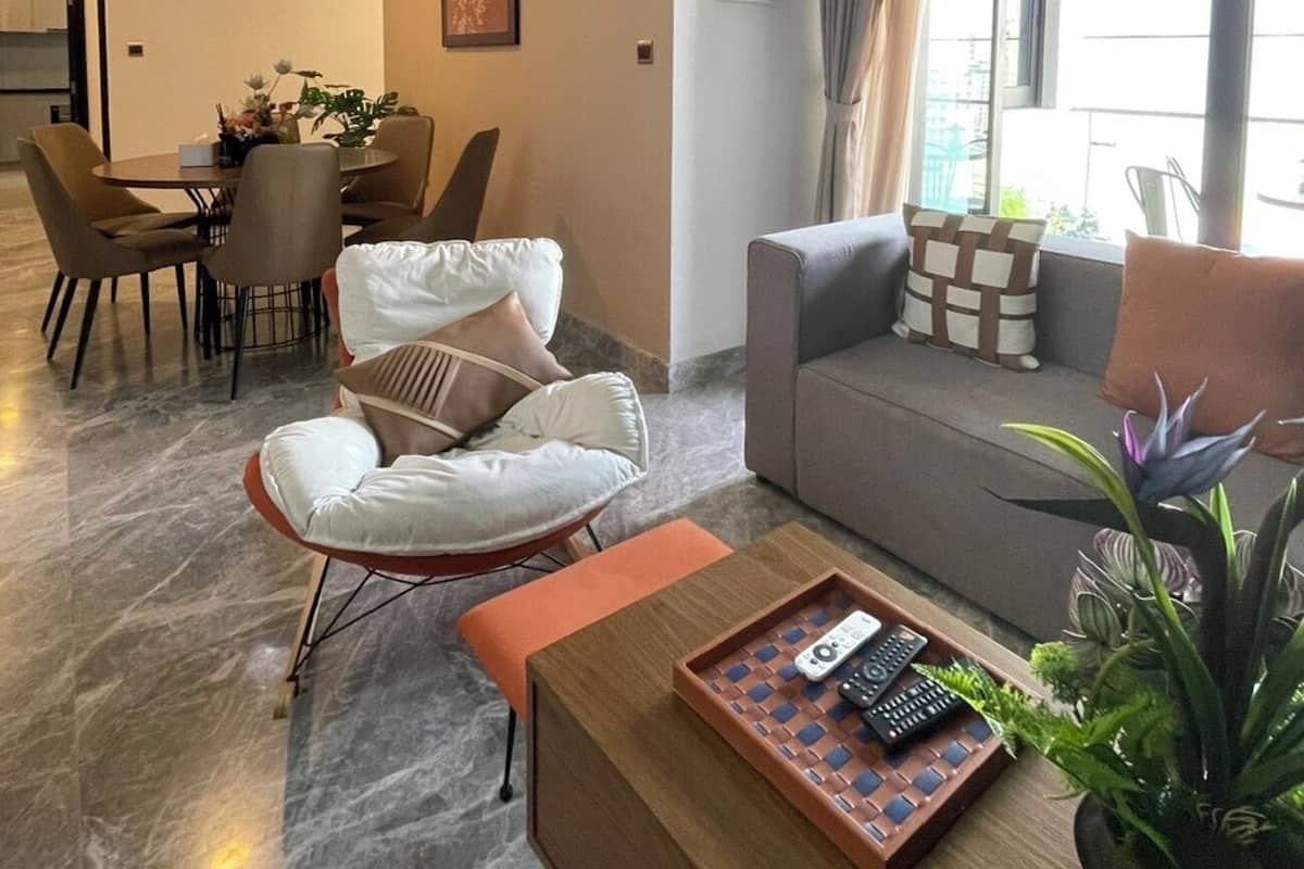 A modern living room with a sofa, armchair, dining table, and a large window with curtains.