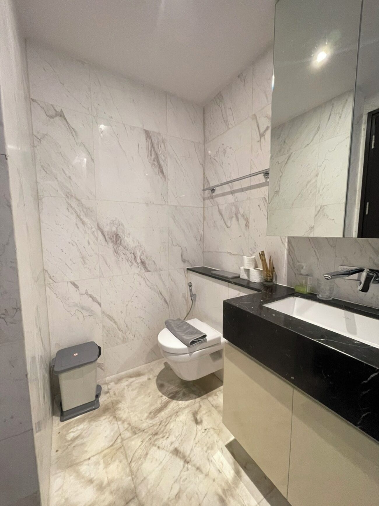 A modern bathroom with marble walls, a black countertop, a white sink, and a toilet.