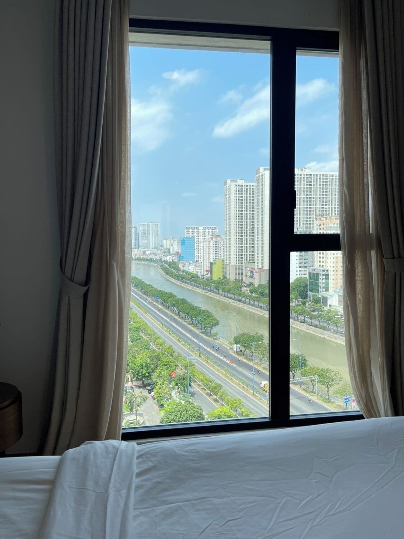 Une chambre d’hôtel avec une grande fenêtre donnant sur le paysage urbain, un lit et des rideaux.