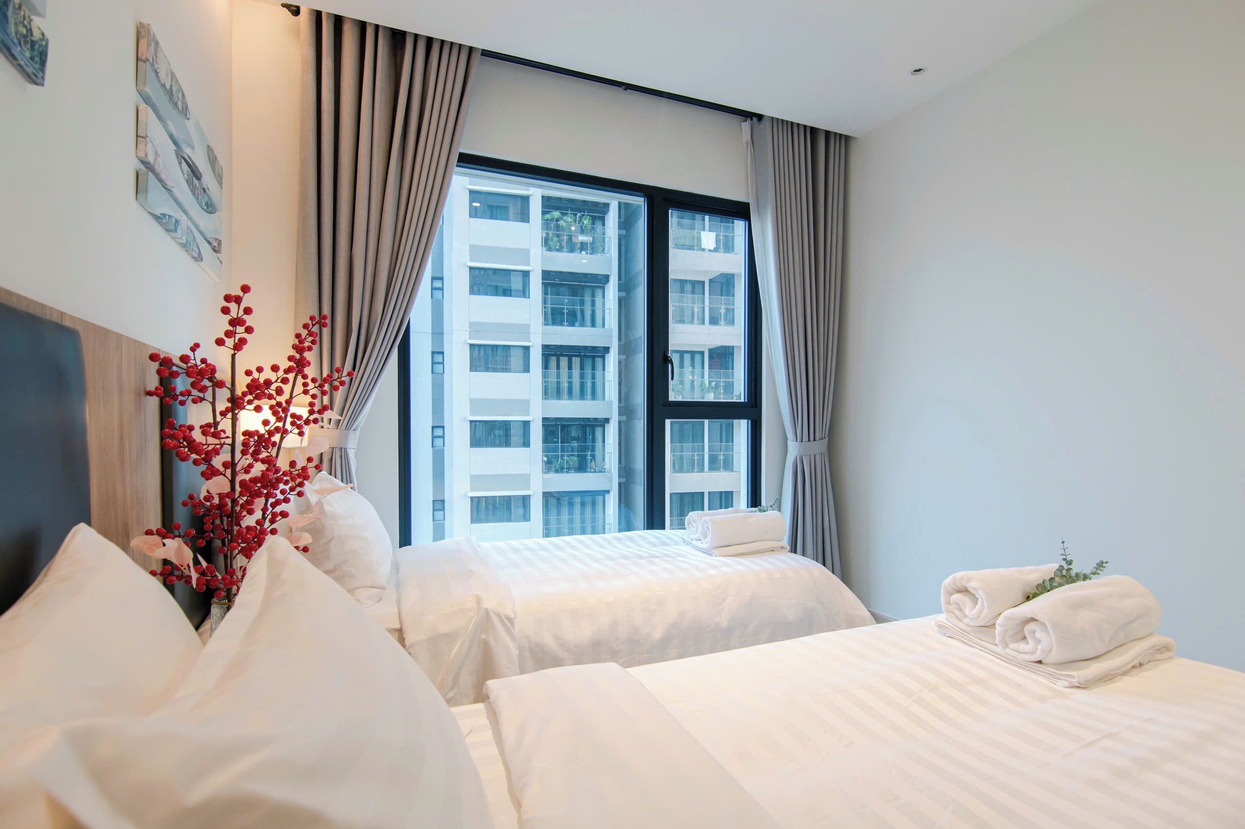 Habitación de hotel con dos camas, un ventanal grande y un florero con bayas rojas.