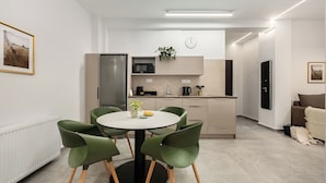 A modern kitchen with a dining area, featuring a round table with chairs, a refrigerator, microwave, and a clock on the wall.