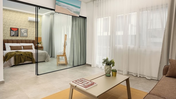 A modern hotel room with a bed, a desk, a chair, a painting, and a view of the beach through a glass door.