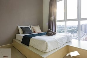 Un dormitorio moderno con una cama, almohadas y vistas de la ciudad a través de amplias ventanas.