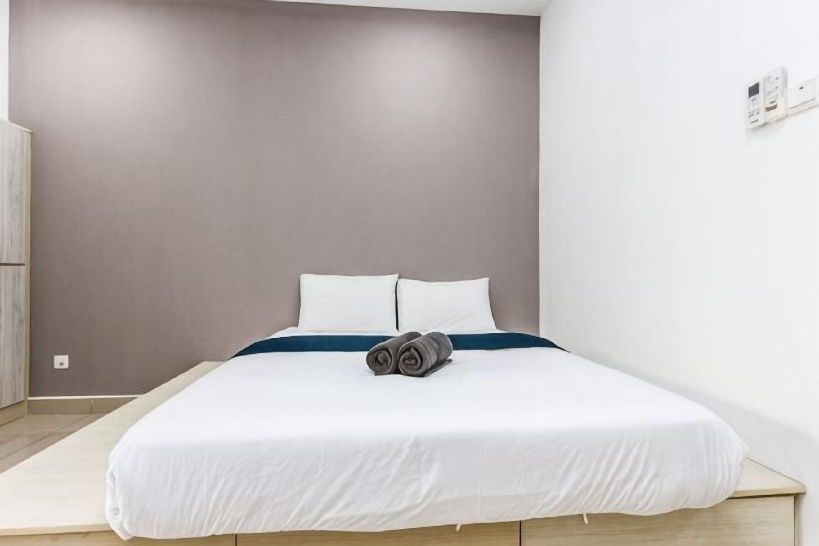 Ein Einzelbett mit weißer Bettwäsche und blauem Akzent, eine graue Wand und ein Holzboden.