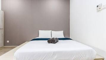 Ein Einzelbett mit weißer Bettwäsche und blauem Akzent, eine graue Wand und ein Holzboden.