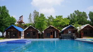 Un espace piscine agrémenté de cabanes en bois et d’un élément décoratif aquatique.