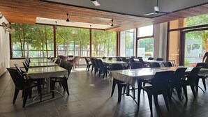 Un vaste espace intérieur aménagé en salle à manger, doté de grandes fenêtres, d’un plafond en bois et de mobilier moderne.