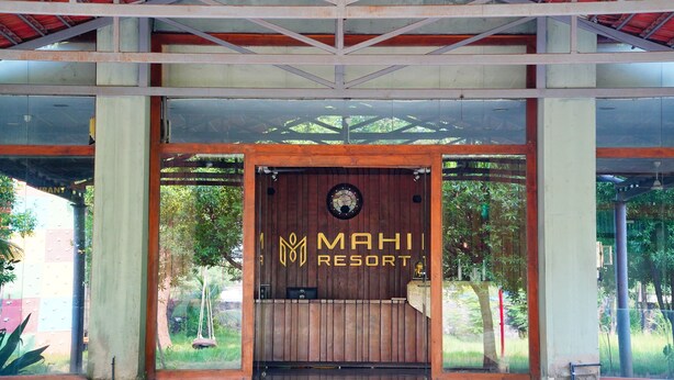 Une entrée en bois avec une enseigne indiquant « MAHIT RESORT » et une horloge au-dessus de la porte.