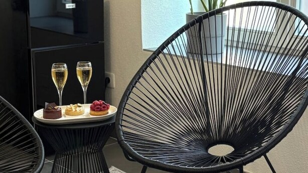 A modern room with a black chair, a small table with two glasses of champagne and desserts, and a black cabinet.