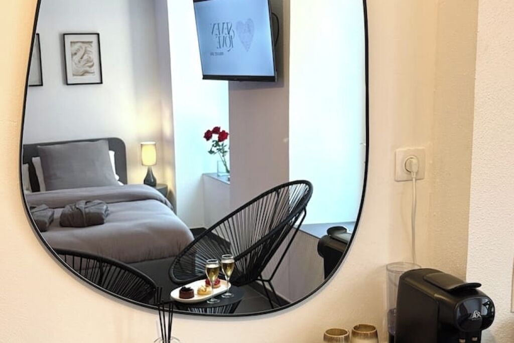 A bedroom with a bed, a chair, a table with a tray of food and drinks, a TV, and a flower vase.